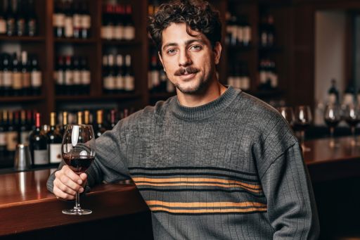 This man in a wine bar setting, moody ambient lighting, relaxed pose leaning on bar, confident alluring expression