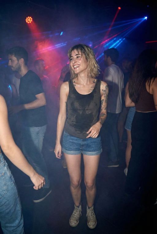 This caucasian young woman is wearing sweaty tank top and shorts, at a rave in a dark night club, polluted air, full body shot, wearing sneakers